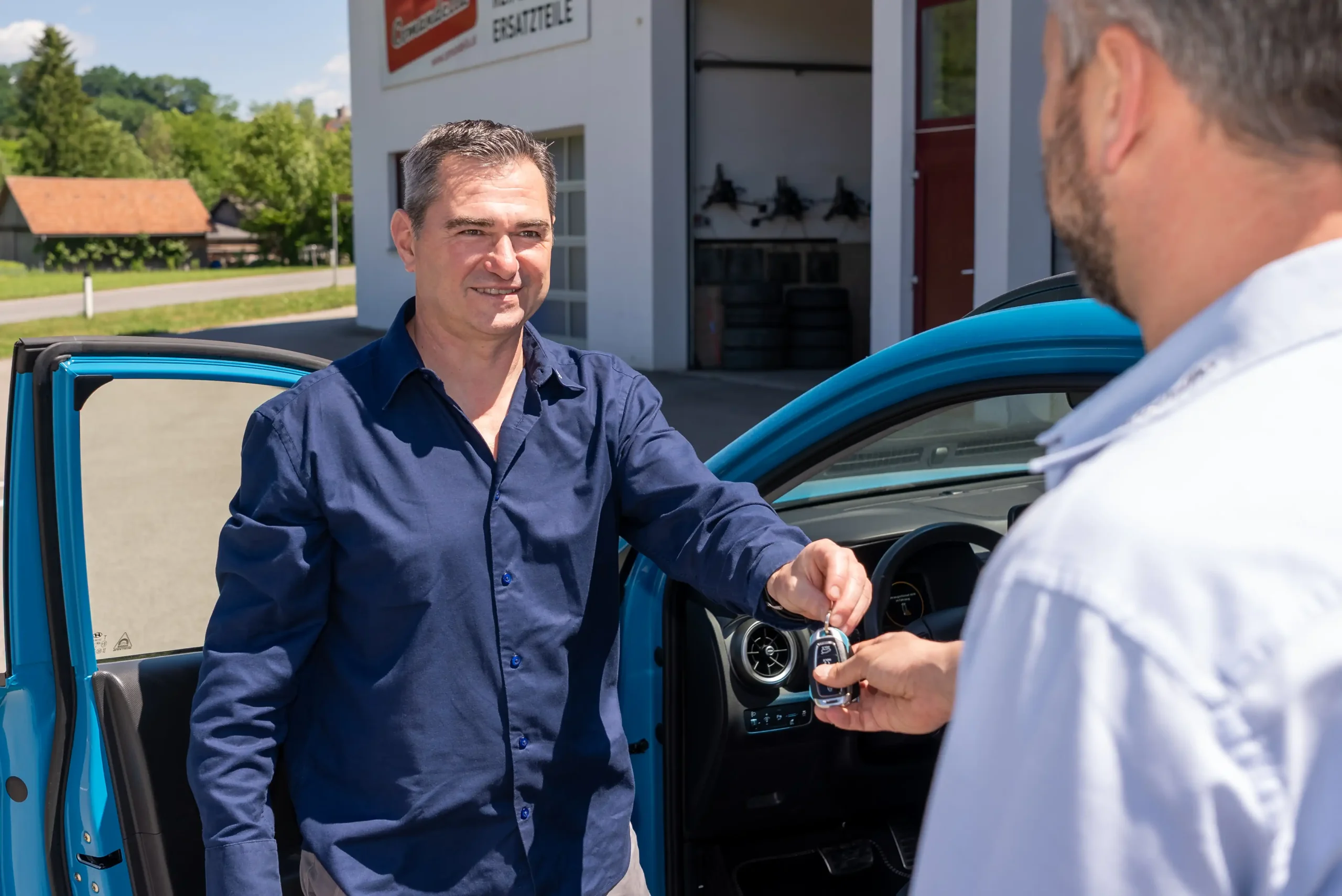 Ein freundlicher Mitarbeiter des Autohauses Comandella bekommt den Schlüssel von einem Kunden ueberreicht nach einem Fahrzeugankauf.